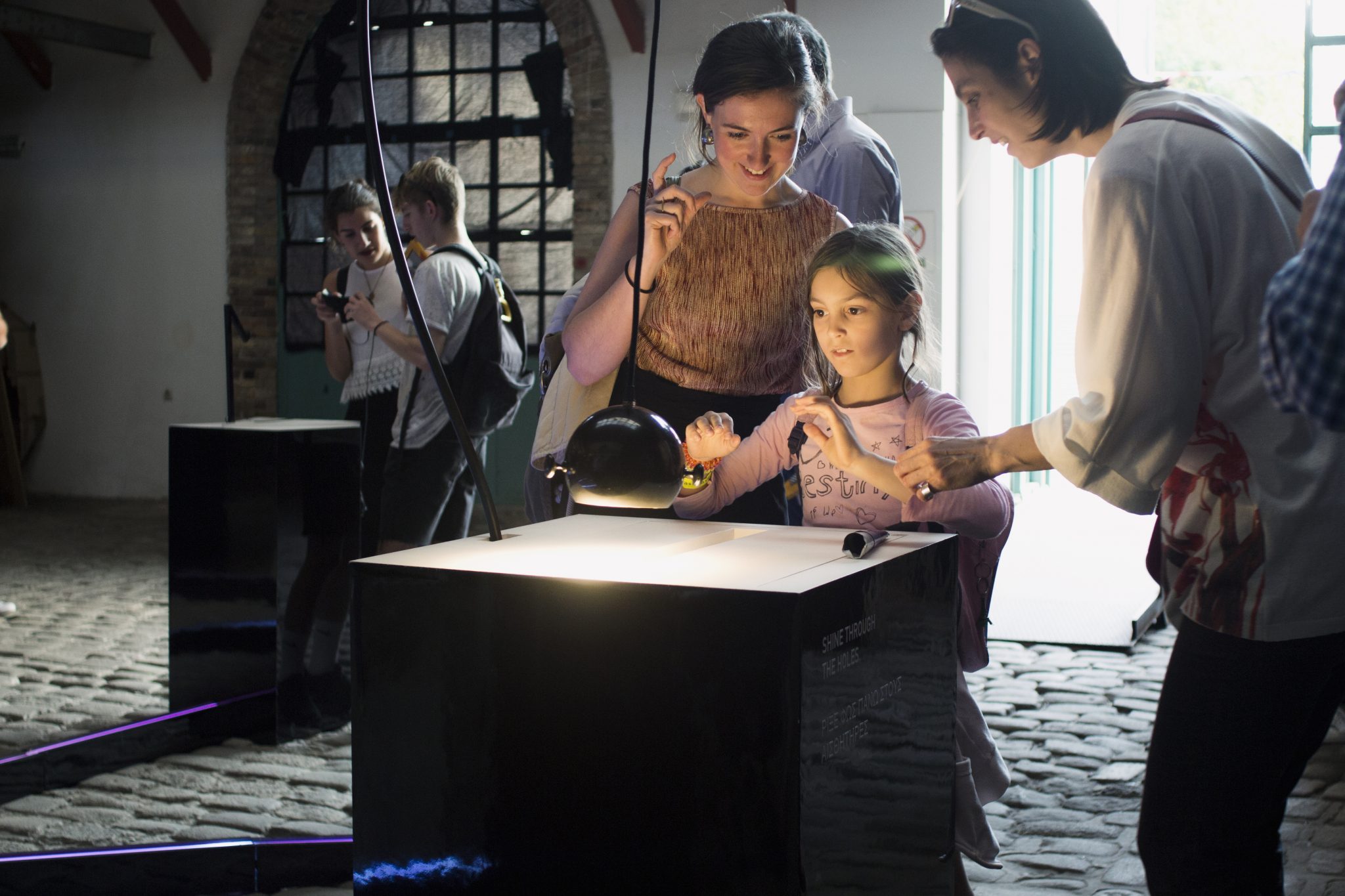 A child and two adults explore an illuminated instrument using handheld lamps.