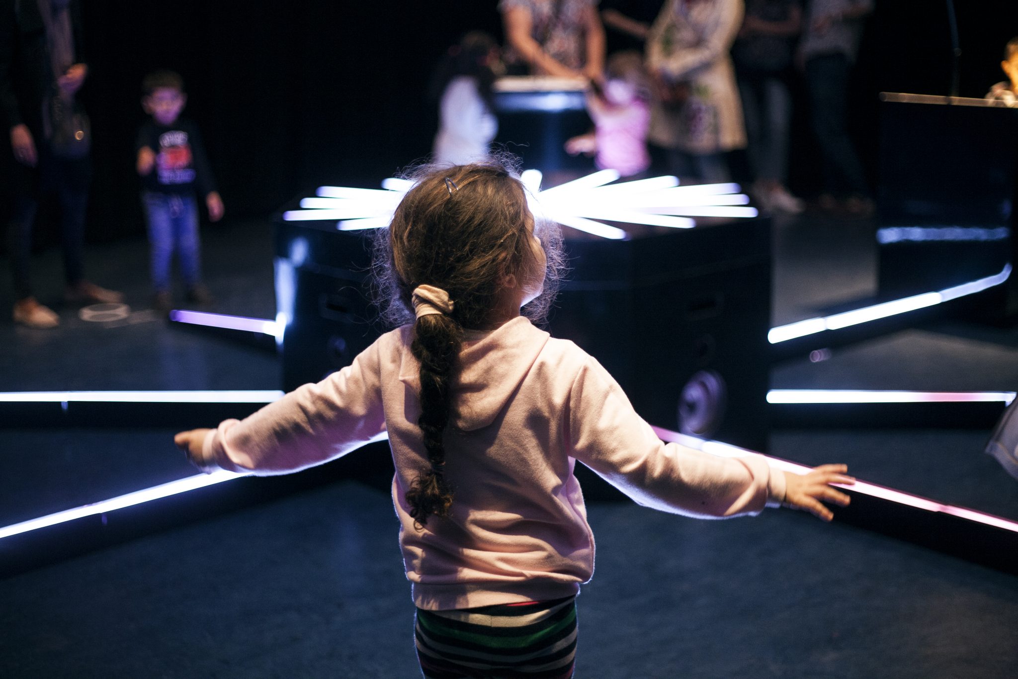 A child plays with arms outstretched beside the glowing hub and instruments.